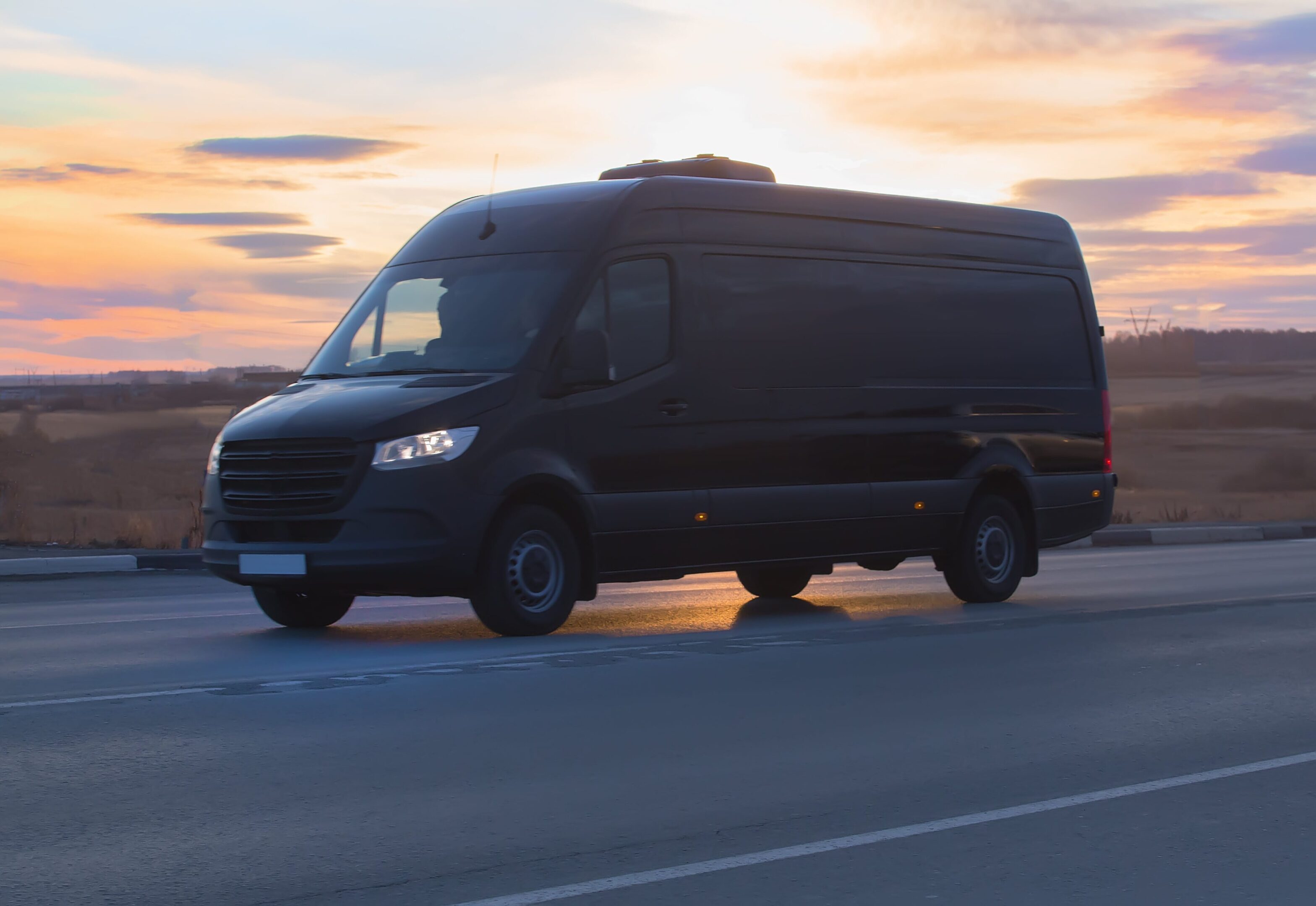 A black delivery van driving on a highway at sunset.