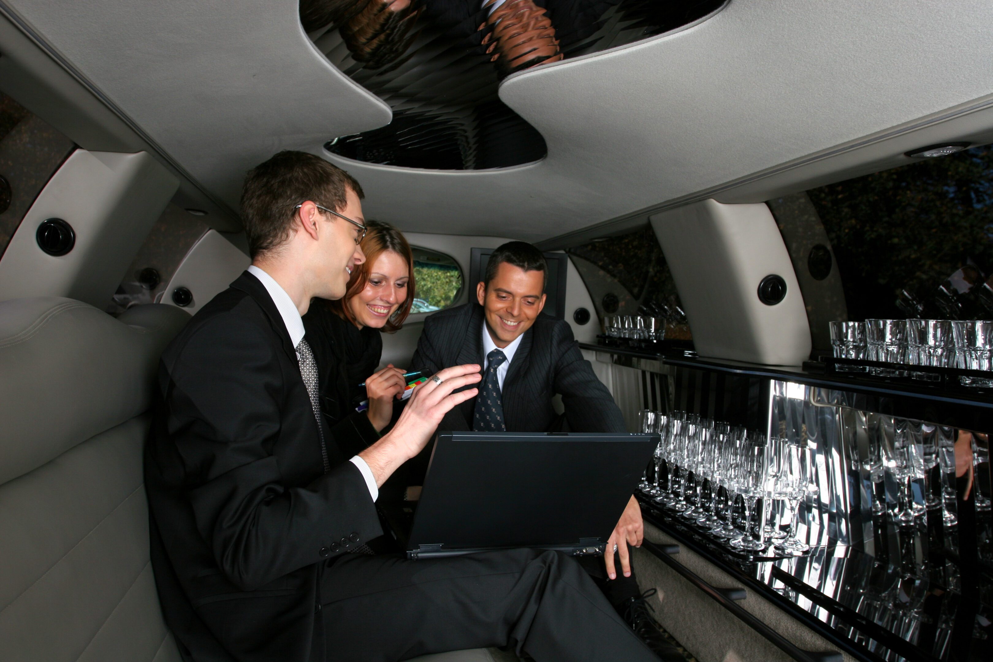 Three business people in limousine. Happy looking on laptop computer.